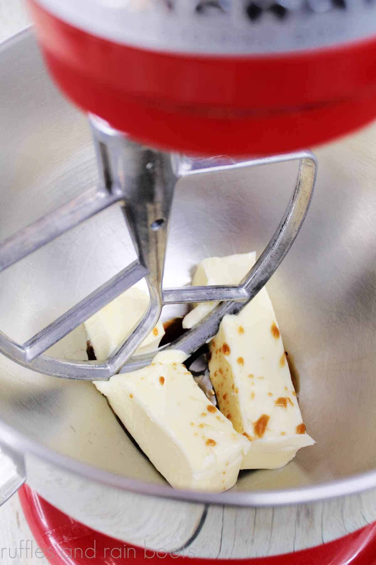 Vertical image of Irish butter and vanilla extract in bowl of red stand mixer with paddle attachment.
