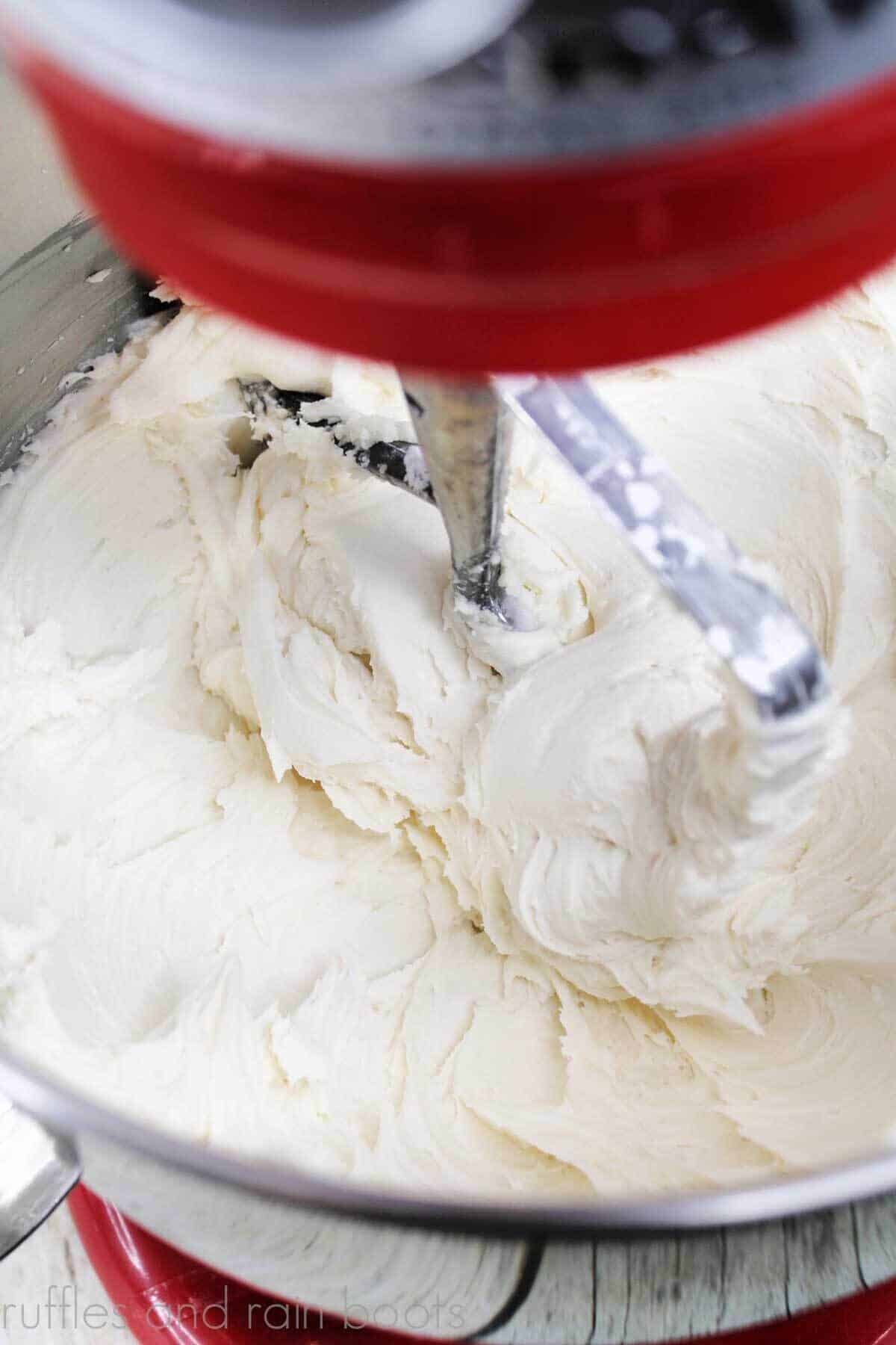 Vertical image of red stand mixer and paddle combining cream into the buttercream frosting recipe.