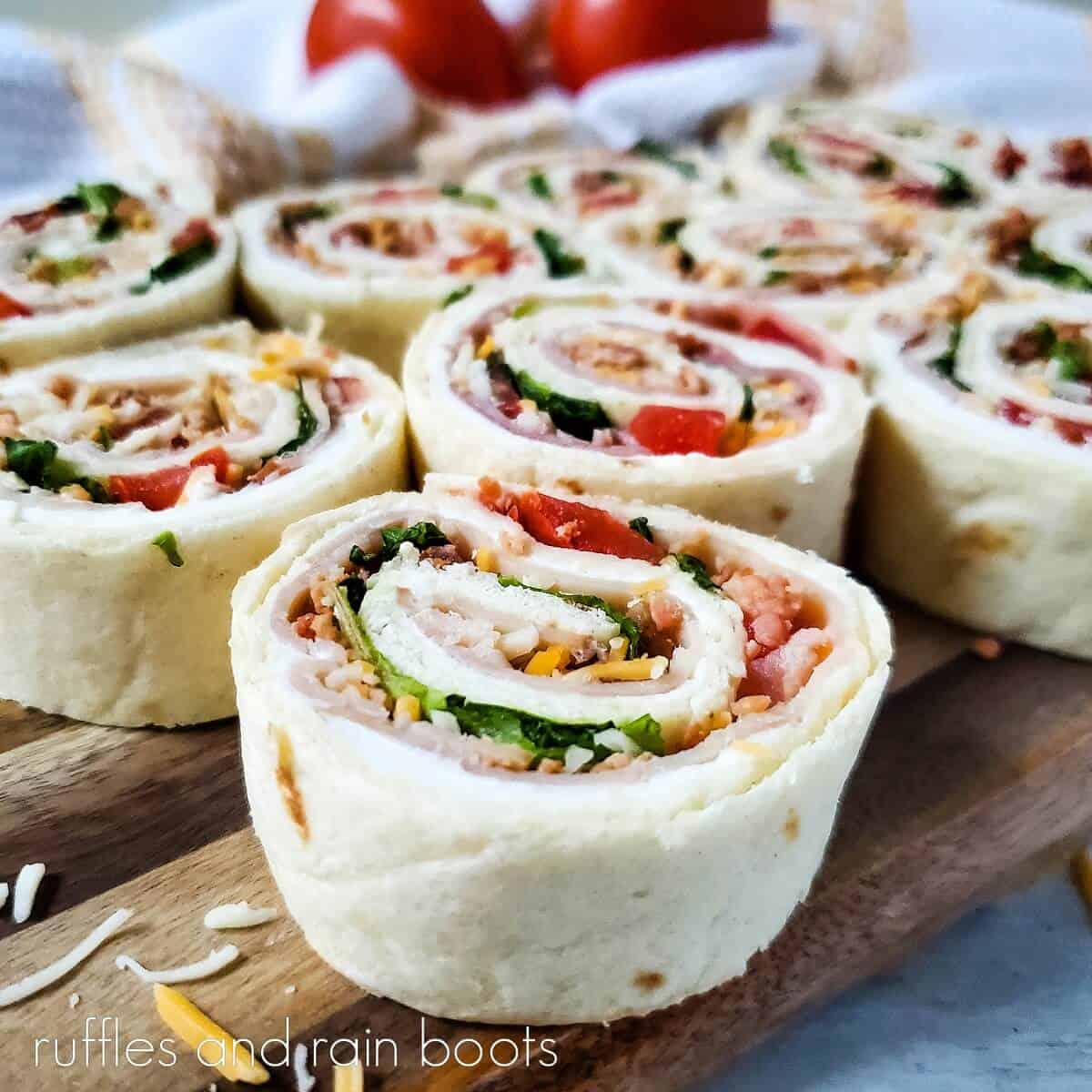 Close u of the rolled Club Sandwich Pinwheels Recipe on a wooden cutting board on a marble surface.