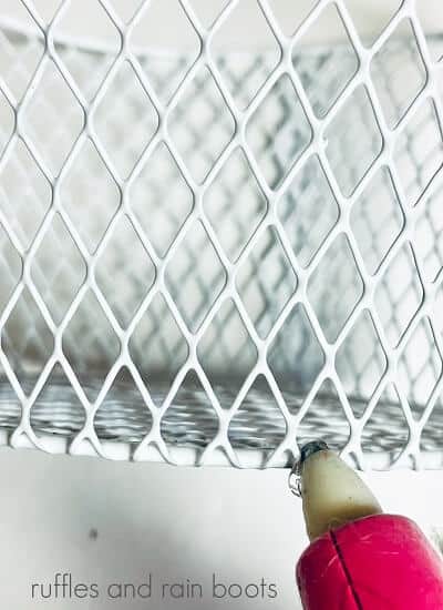 Close up of a pink hot glue gun putting glue on a white metal basket on a white background
