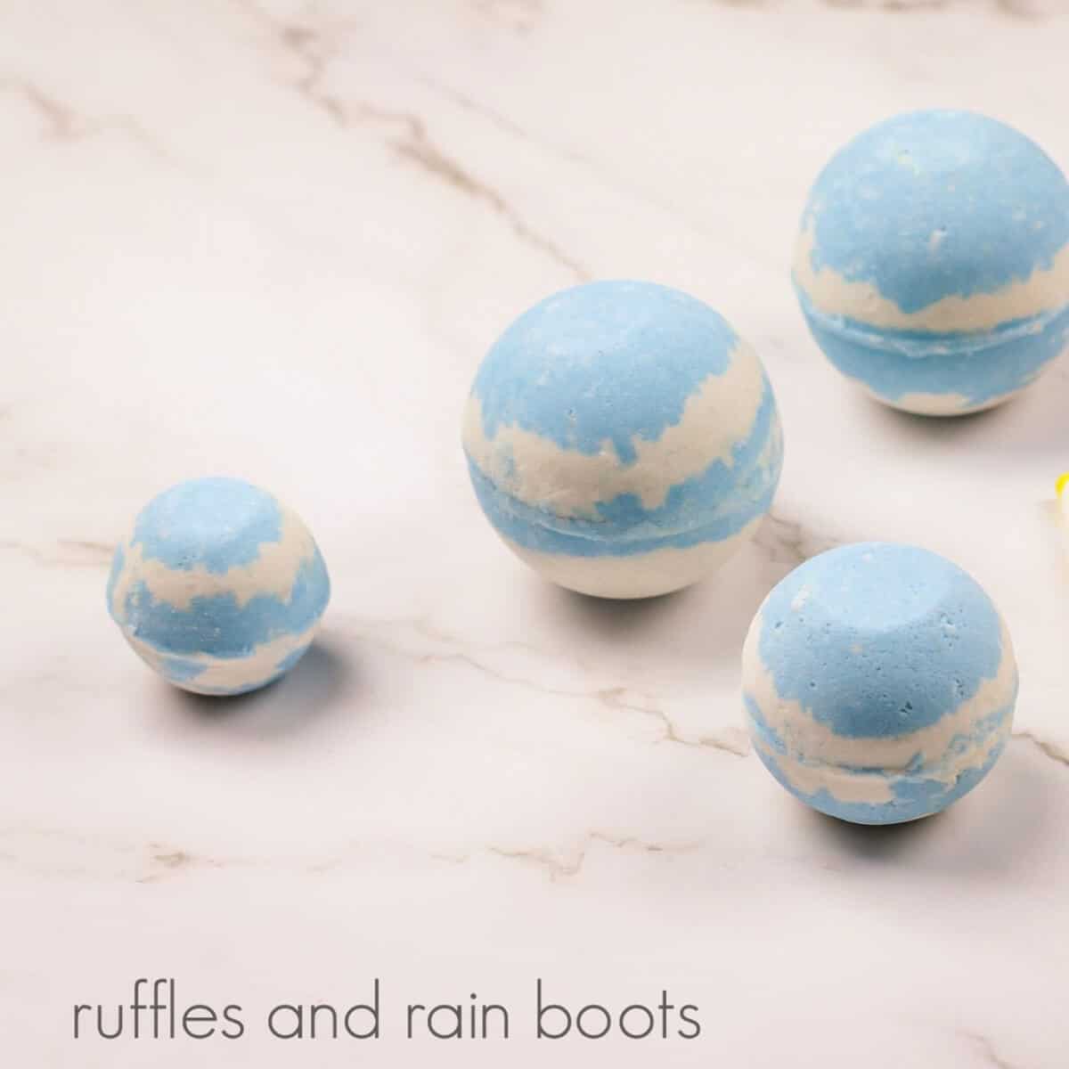3 large and 1 small blue and white bath bombs, on a white marble background.