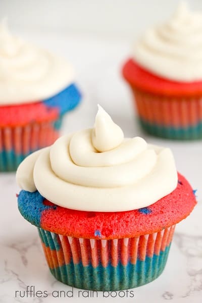 Close up of a frosted USA cupcakes with 2 other cupcakes in the background on a white marble surface.