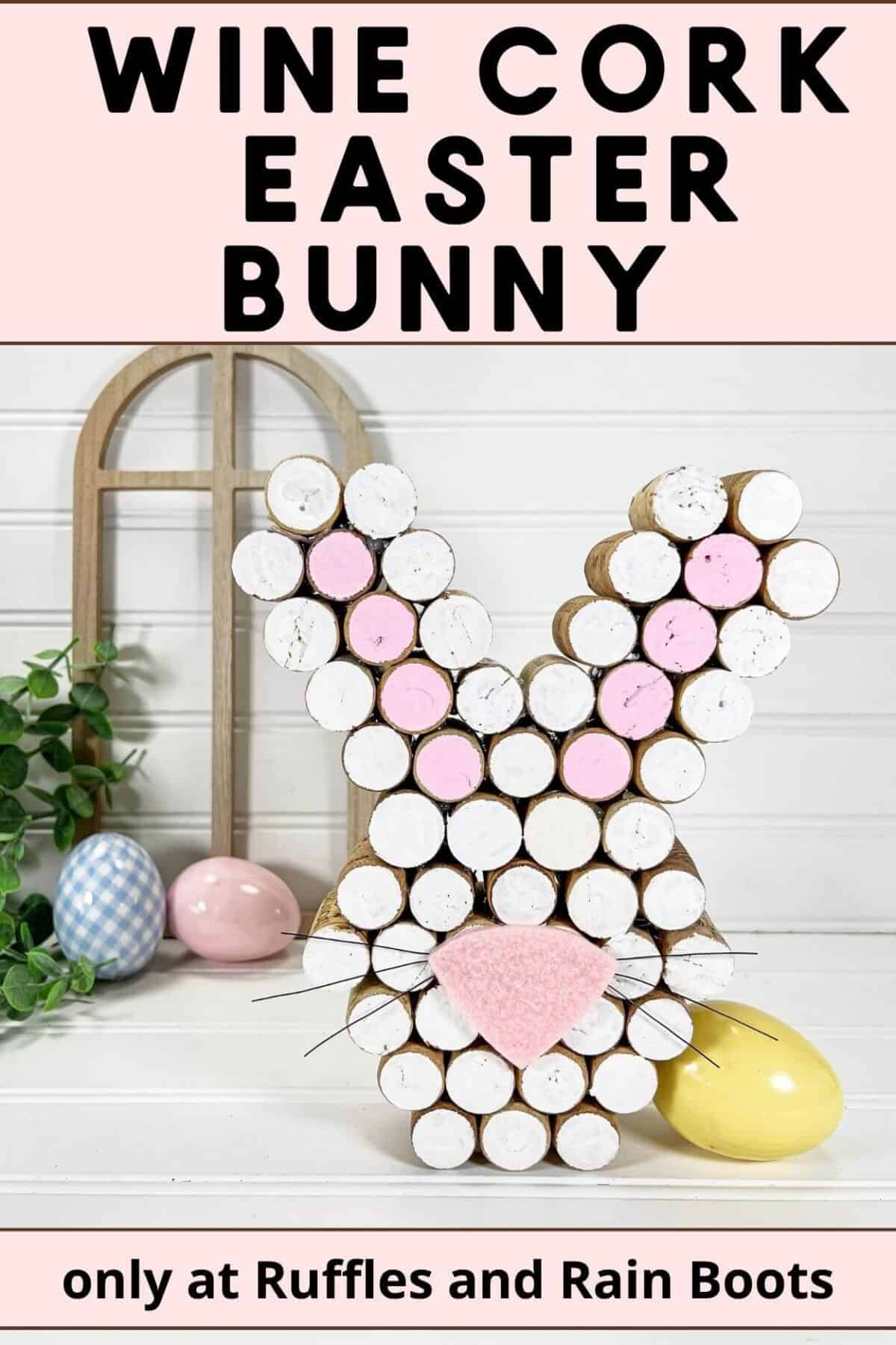 Vertical pin image with a painted Recycled Wine Cork Easter Bunny Craft with faux greenery, a wooden arch, and decorative Easter Eggs in the background on a white surface.