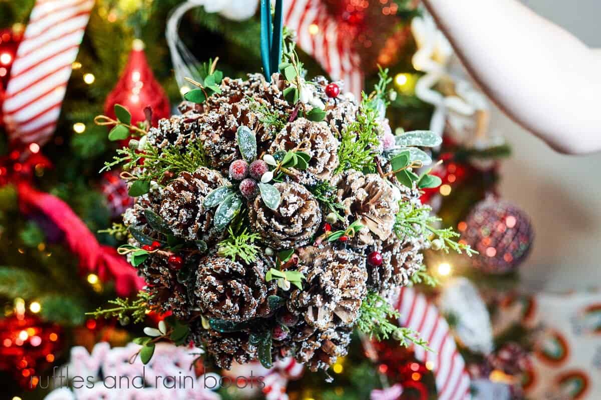 This elegant and easy DIY pinecone kissing bal is a traditional decoration that gets a remake for your home this Christmas. Also called a pomander, you can add a fragrance or perfume to make the house smell amazing and even add lights! Use this holiday craft for parties, easy decor, or a fun Christmas craft idea. It works with artificial or live greenery and is so simple, you can make it in minutes with a handful of supplies. 