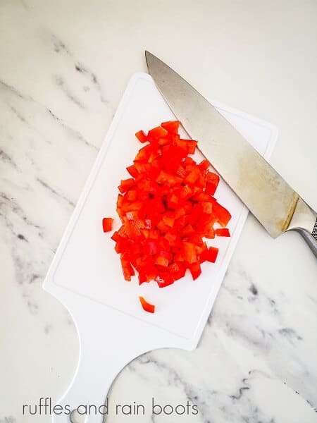 Cut red peppers, next to a small knife on a white cutting board on a white marble background.