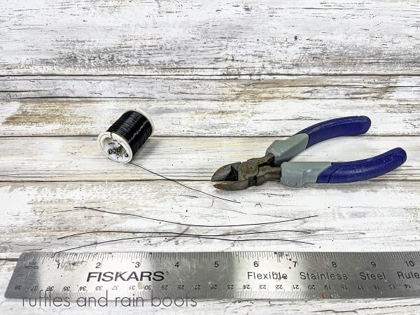 Black wire next to a metal ruler and a wire cutter on a white weathered wood surface.