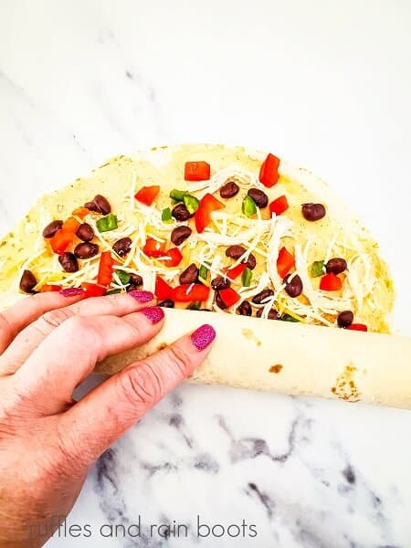 Mexican fiesta pinwheel sandwiches on a white marble background being rolled by someone’s hand.