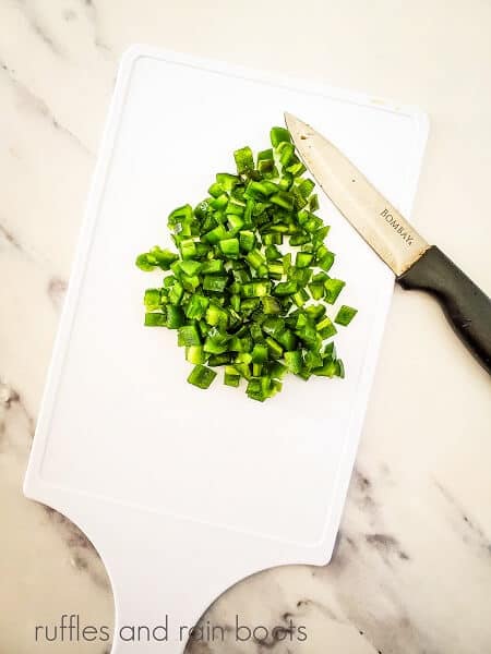 Cut green peppers, next to a small knife on a white cutting board on a white marble background.