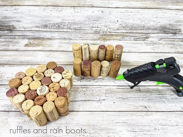 Groups of glued recycled wine corks next to a hot glue gun on a white weathered wood surface.