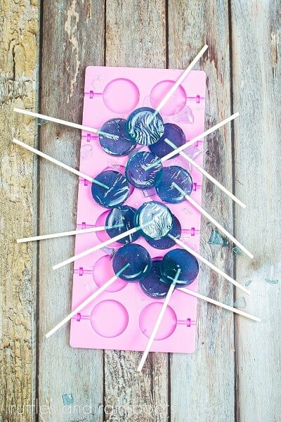 a silicone lollipop mold filled with blueberry lollipops on a weathered wood surface.