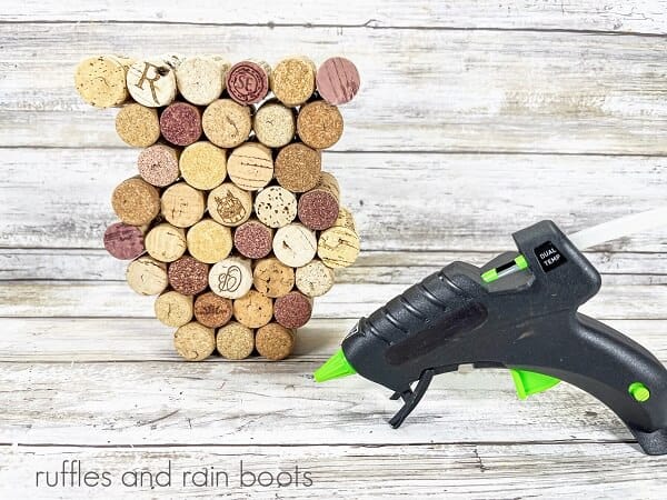 A group of glued recycled wine corks next to a hot glue gun on a white weathered wood surface.