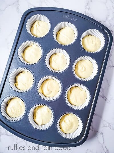 A cupcake pan filled with liners filled with cake batter against a white marble background.