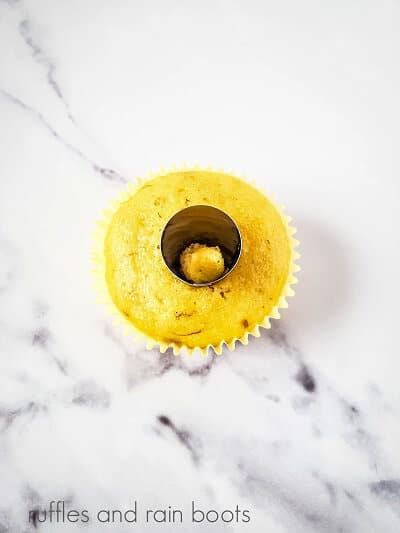 One cupcake with a hole bring cut out with a large frosting tip on a white marble background.