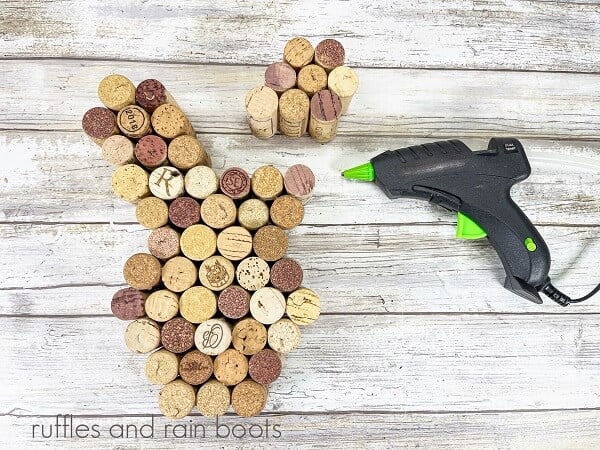 An unpainted Recycled Wine Cork Easter Bunny Craft next to a hot glue gun on a white weathered wood surface.