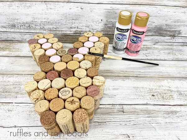 An unpainted Recycled Wine Cork Easter Bunny Craft next to two bottles of acrylic paint and a paintbrush on a white weathered wood surface.