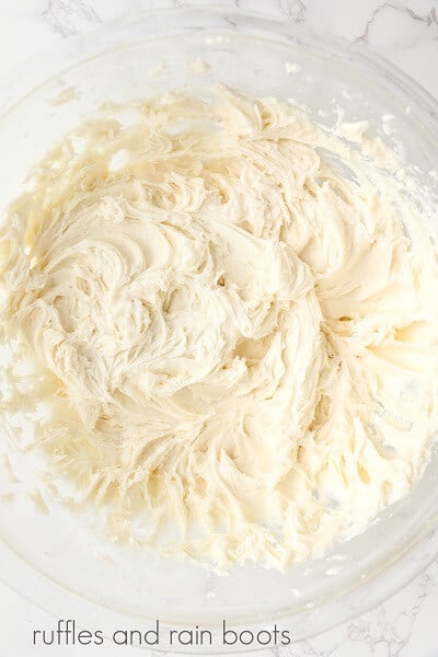 A round glass bowl of vanilla frosting on a white marble surface