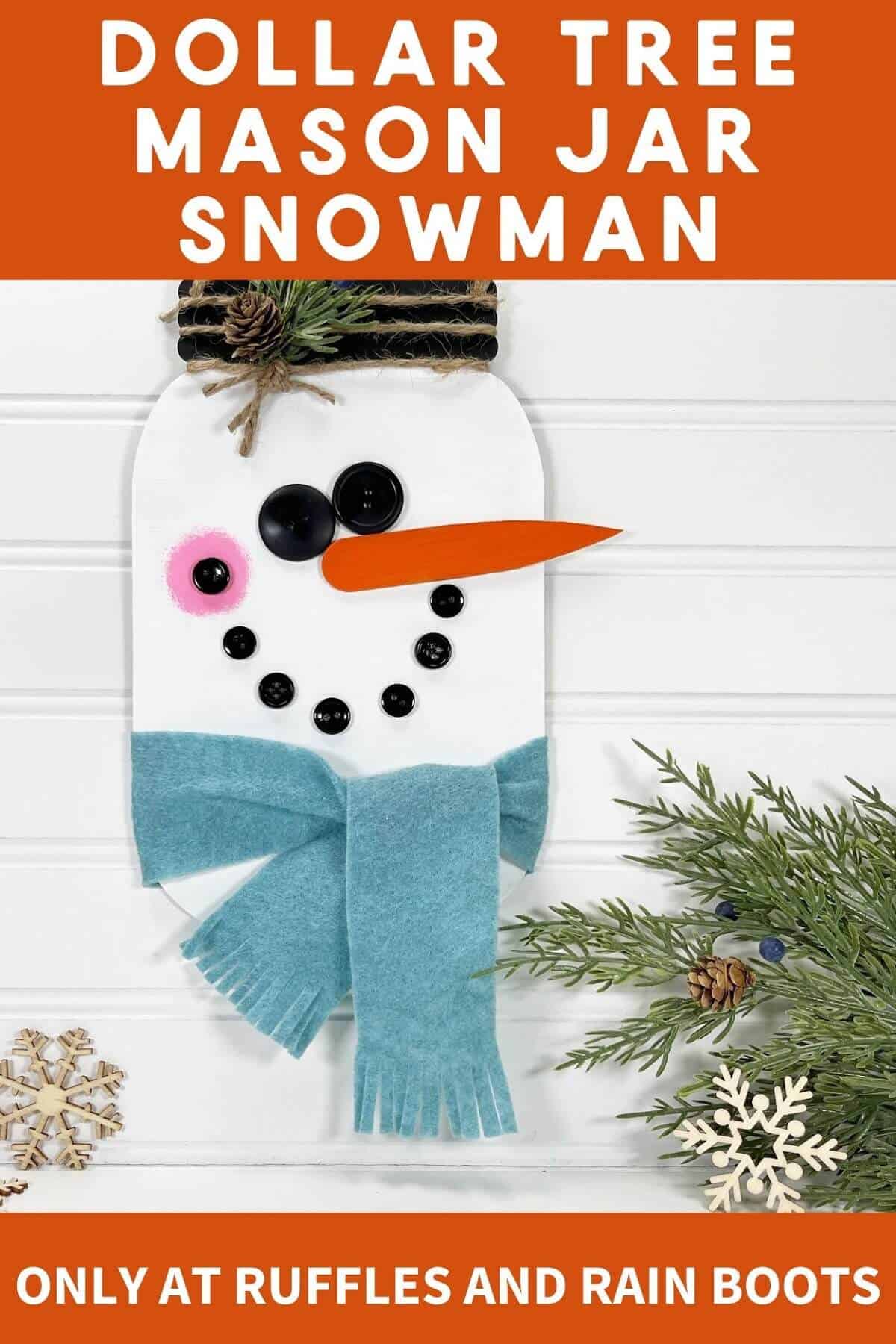 vertical image of a painted galvanized metal Hanging Mason Jar Snowman next to a piece of faux greenery and 2 wooden snowflakes on a white beadboard background