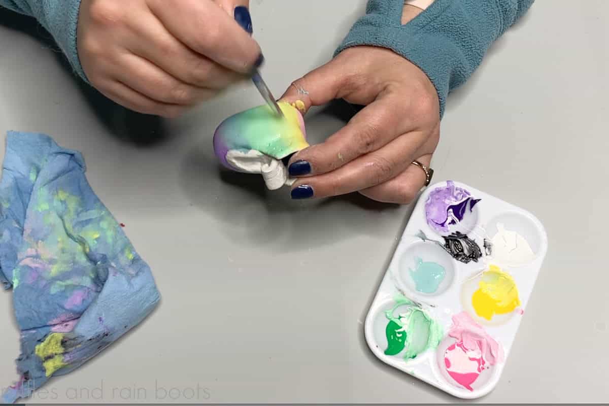 Crafter painting an ombre rainbow in acrylic paint on air dry clay gnome boots.