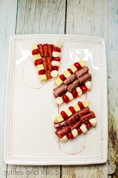 A candy cane shape drawn on a white plate with meats and cheeses against a white weathered wood backdrop.