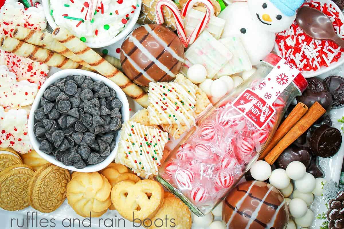 Vertical Christmas hot cocoa charcuterie board filled with snowball whoppers, sprinkles, cookies, marshmallow snowmen and any more sweets on a white plate.