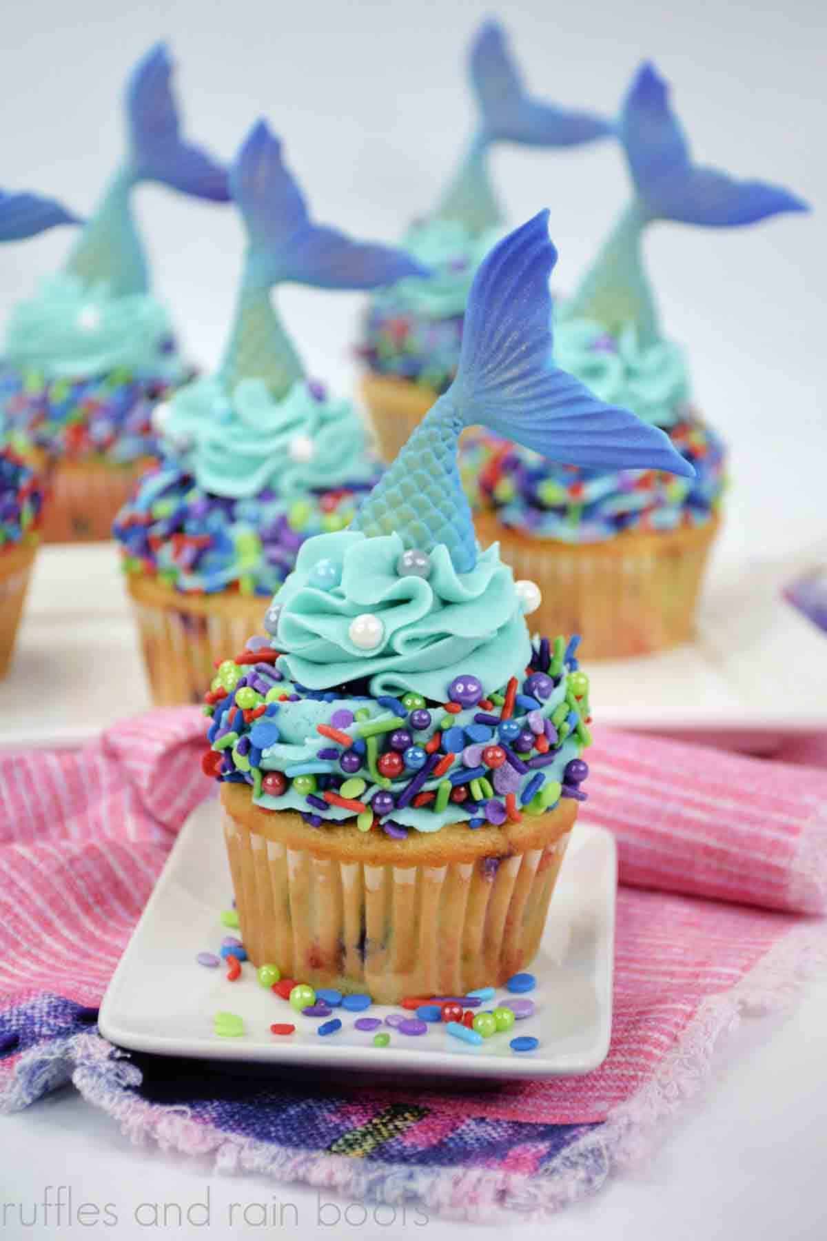 Vertical image of 6 mermaid cupcakes with funfetti cupcake recipe, buttercream frosting, sprinkles, and fondant mermaid tails.