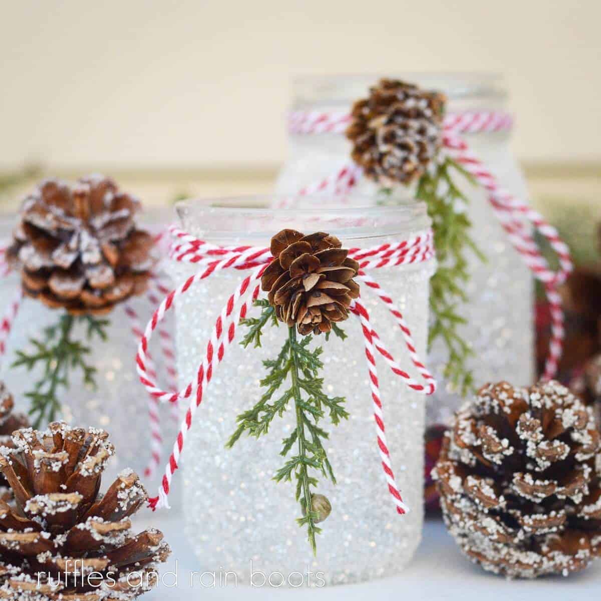a square photo mage of a trio of completed snowy pinecone mason jars next to faux pinecones