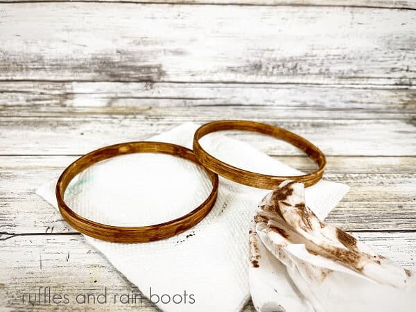 Two wooden hoops painted with brown paint on top of a paper towel, next to a baby wipe, against a white weathered wood background.