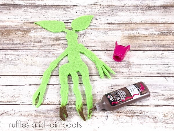 Bowtruckle Felt Bookmark Craft next to a bottle of fabric paint against a white weathered wood background.