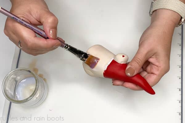 Crafter using a paint brush to apply a liquid sealant to an air dry clay gnome.