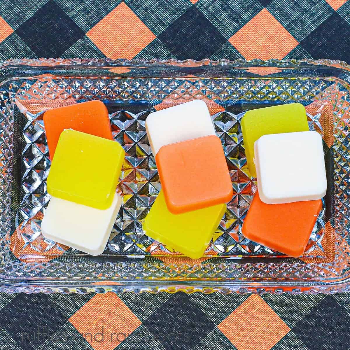 Several Candy Corn Sugar Scrub Cubes on a glass dish against a black and orange background.