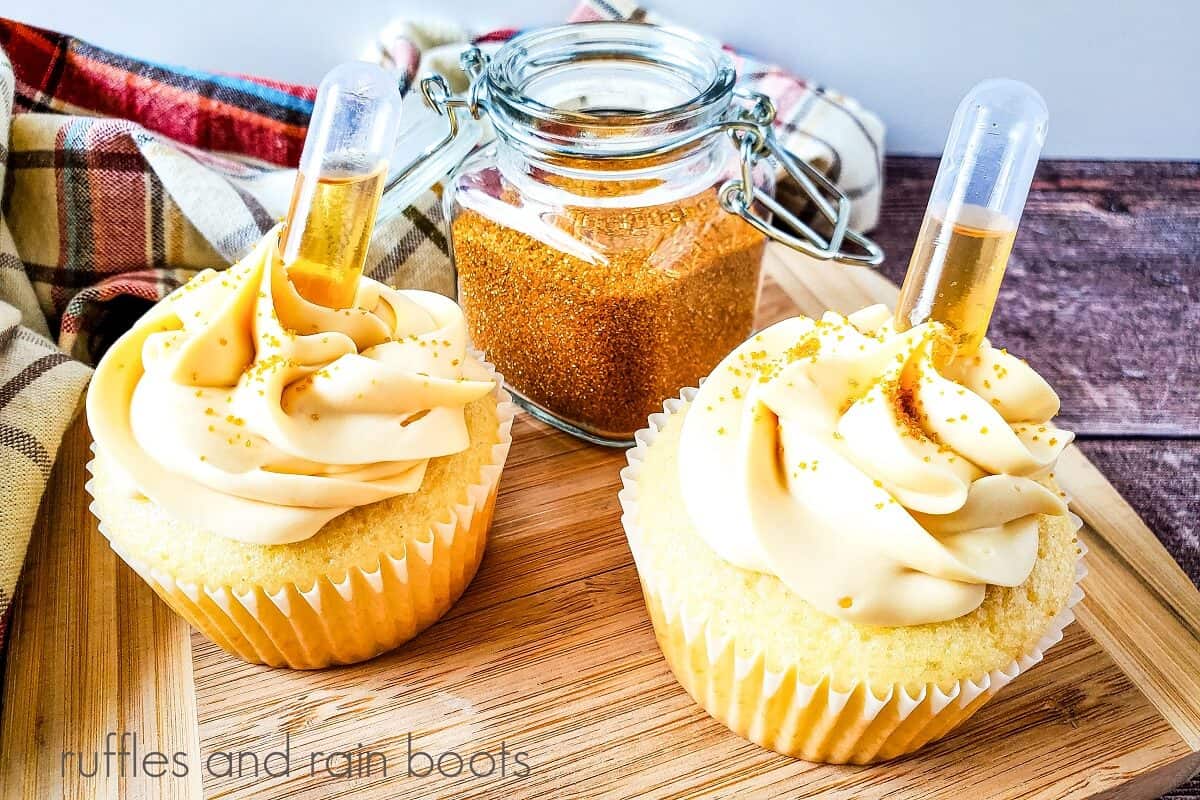 Two cognac cupcakes on a wooden cutting board next to a plaid towel against a weathered wood background.