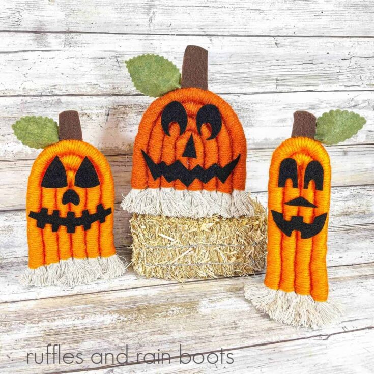 A square of three rope jack-o-lanterns, the small one on the left and the tall one on the right with the middle one on tope of a small bale of hay against a white weathered wood background.