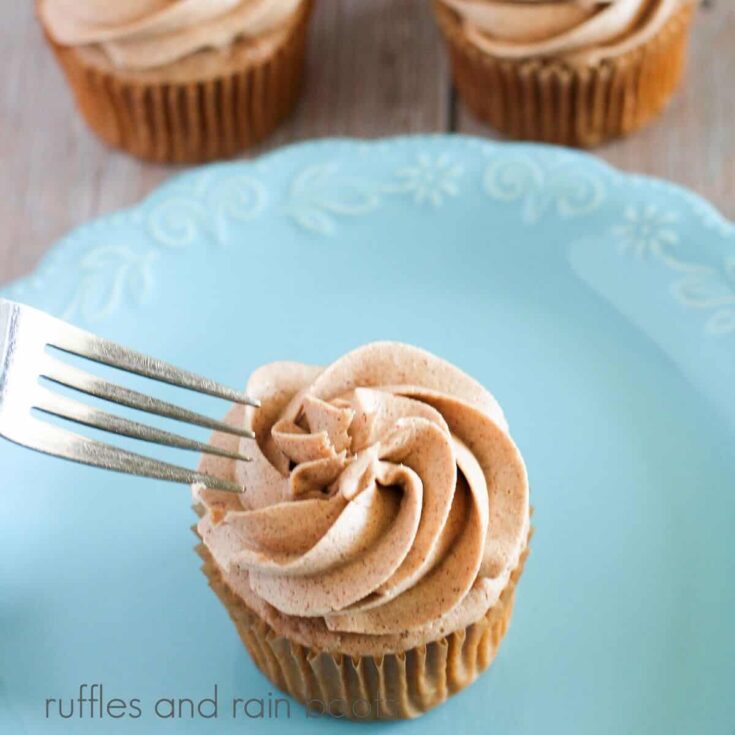 A square image of a blue plate with a frosted snickerdoodle cupcake with a fork next to the frosting, next to two cupcakes against a weathered wood background.