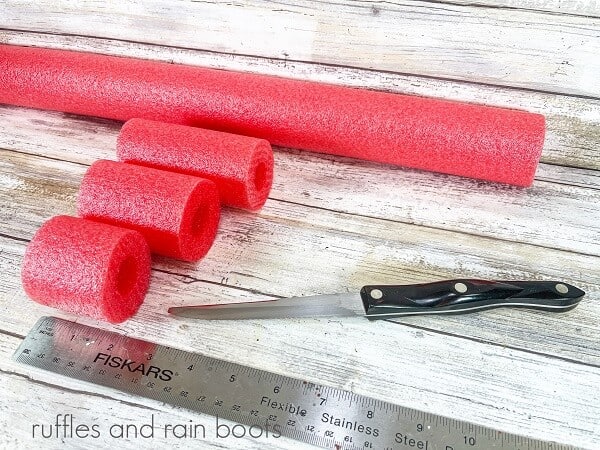 Three cut pool noodles next to a metal ruler and a black handled knife against a white weathered wood background.