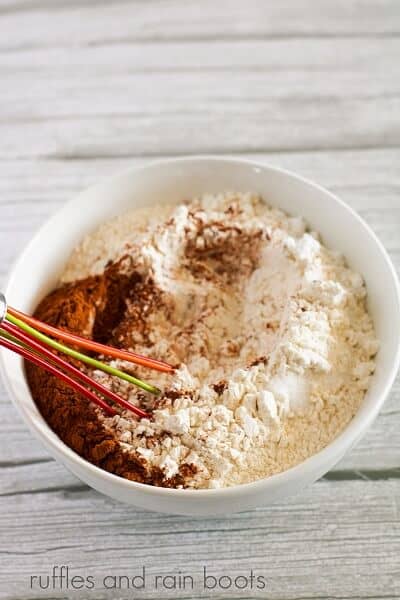 Dry ingredients in a white round bowl with a whisk inside against a white weathered background.