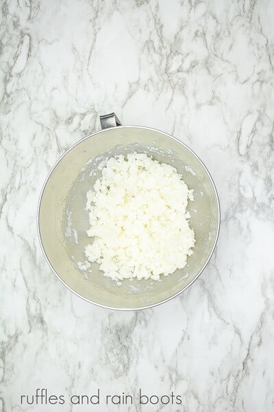 Creamed butter and sugar in a large stainless steel mixing bowl against a white marble background.