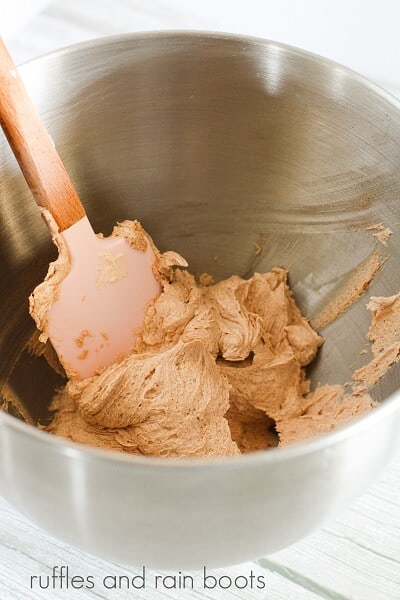 A large metal mixing bowl with a spatula inside, mixing snickerdoodle frosting.