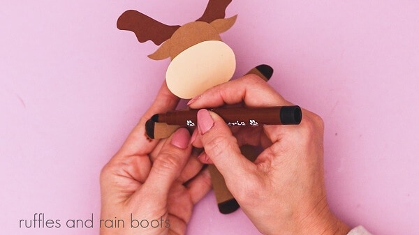 Crafter holding a brown marker coloring in the hooves of the reindeer against a purple background.