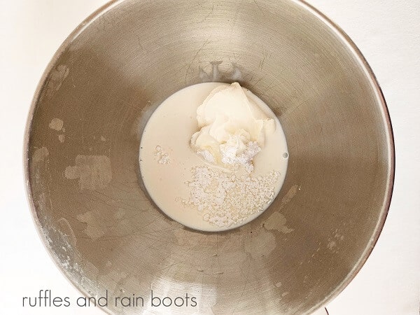 A large metal mixing bowl filled with mascarpone cheese, milk, heavy cream, and powdered sugar against a white background.