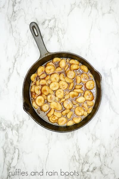 A cast iron skillet with bananas and a brown sugar glaze on a white marble background.