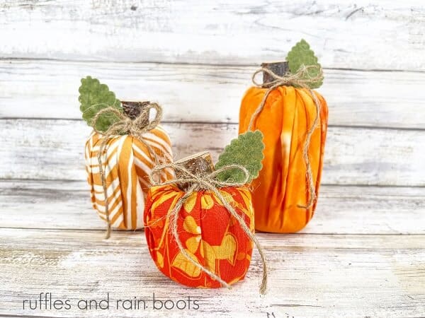 Three wrapped Dollar Store pool noodle pumpkins, one in orange and white, one orange and yellow and one orange against a white weathered wood background