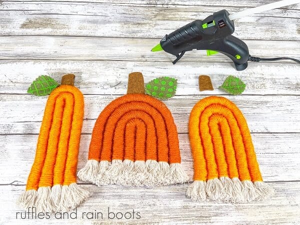 Three rope pumpkins with stems and leaves next to a hot glue gun against a white weathered wood background.