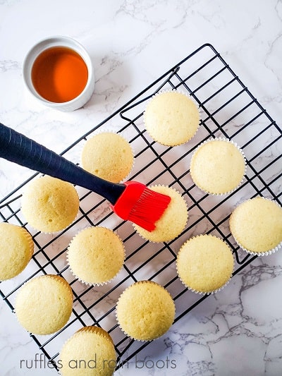 12 unfrosted cupcakes being brushed with cognac against a white marble background.