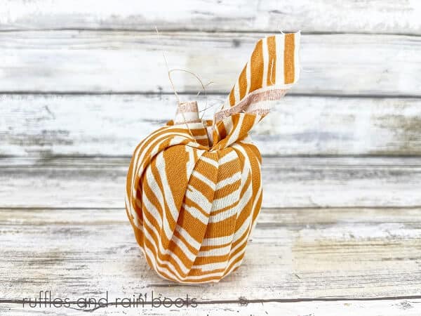 A pool noodle wrapped in orange and white striped fabric against a white weathered wood background.