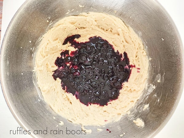 A large mixing bowl filled with vanilla cupcake batter and blueberry puree against a white background.