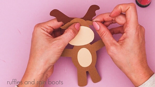 A crafter gluing horns into a reindeer against a purple background.