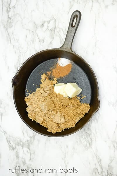 A cast iron skillet with the ingredients for a brown sugar glaze on a white marble background.