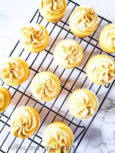 12 frosted cognac cupcakes on a wire cooling rack against a white marble background.