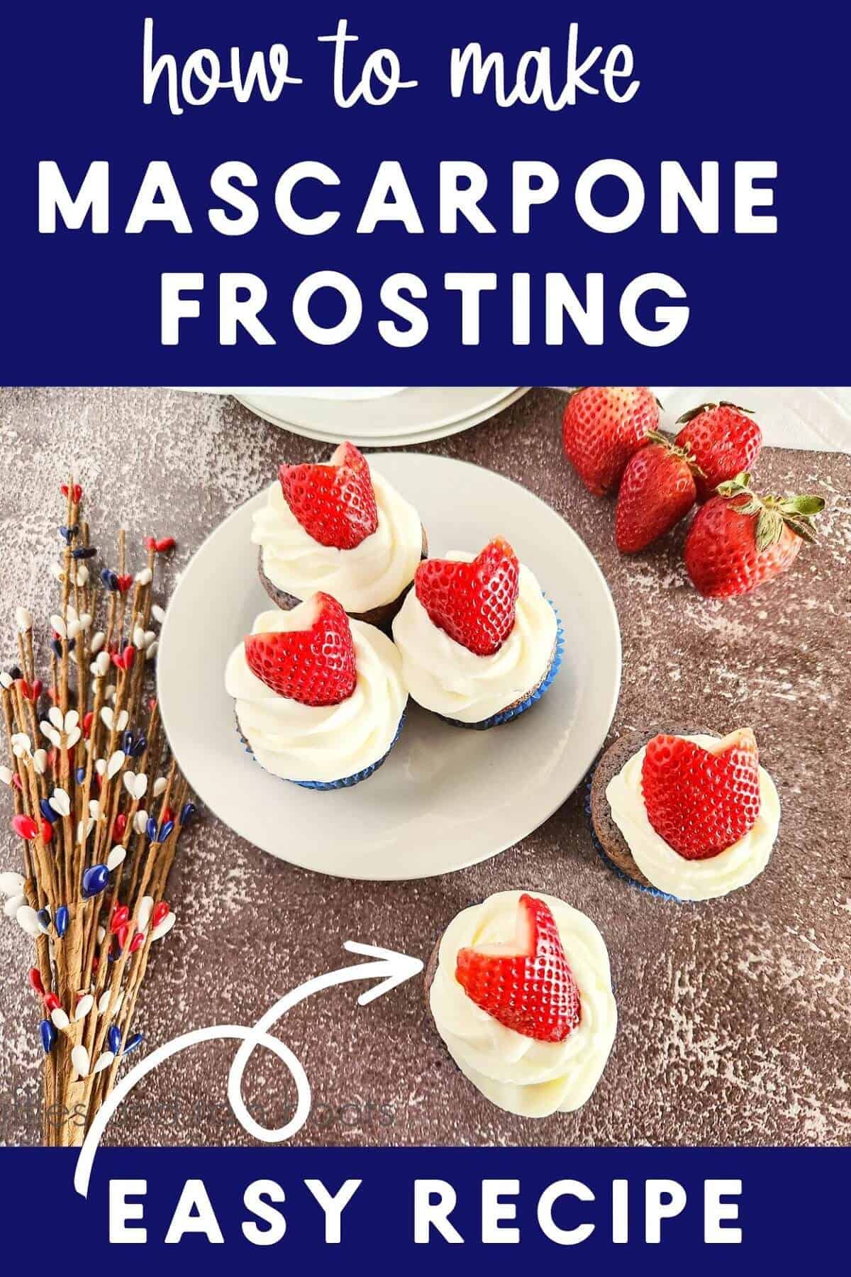 A plate of frosted blueberry cupcakes with strawberries on top, next to 2 other cupcakes and a bunch of fresh strawberries, next to holiday decorations against a brown background.