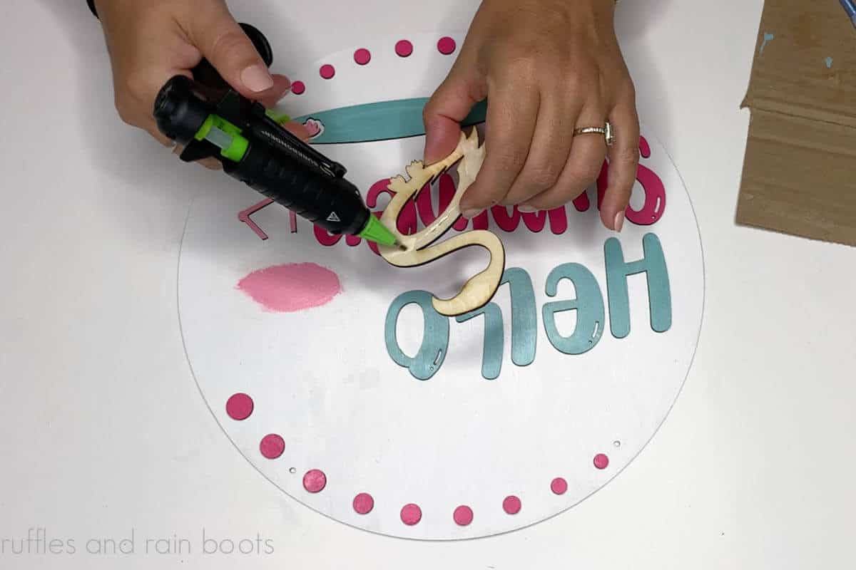 Crafter gluing a flamingo piece to a painted wood round door sign.